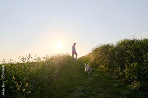 Woman Silhouette with a dog walking up a gravel path at sunset