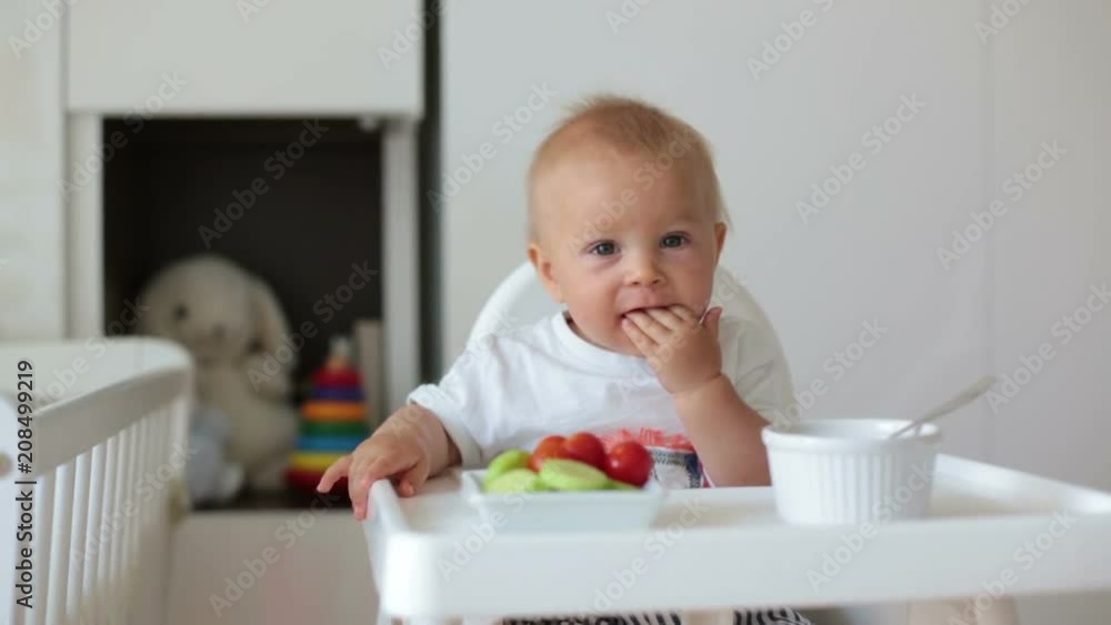Sweet baby child, boy, eating mashed food and fresh vegetables, sitting in high baby chair in kids room Sweet baby child, boy, eating mashed food and fresh vegetables, sitting in high baby chair in kids room