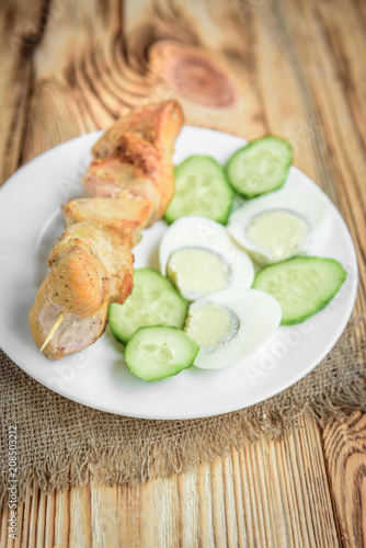 oiled chicken breast with fried eggs and cucumber on white plate on wooden background. Healthy lunch or dinner.