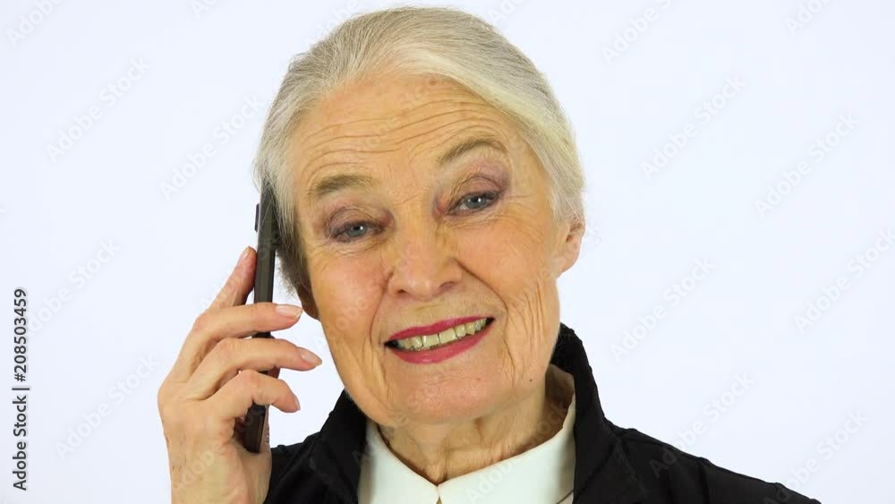 An elderly woman talks on a smartphone and looks at the camera - face closeup - white screen studio An elderly woman talks on a smartphone and looks at the camera - face closeup - white screen studio