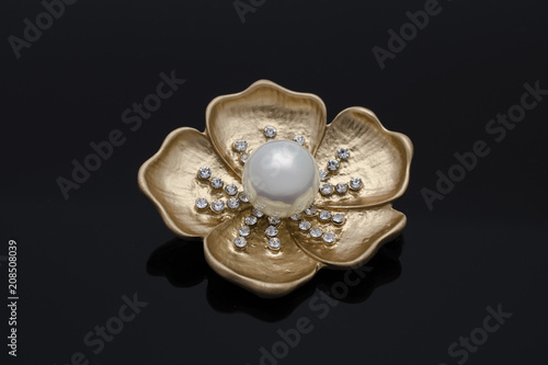 gold brooch flower with a pearl and diamonds isolated on black