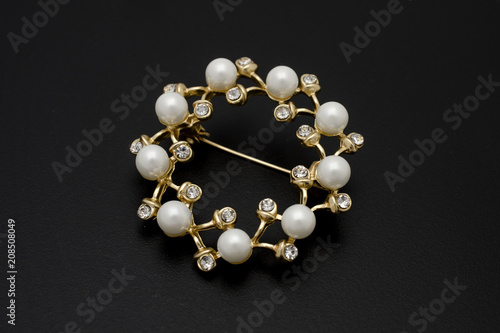 gold round brooch with pearls and gems isolated on black
