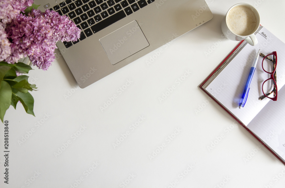 Top view of white desk with laptop, coffee, note book, glasses and lilac Top view of white desk with laptop, coffee, note book, glasses and lilac