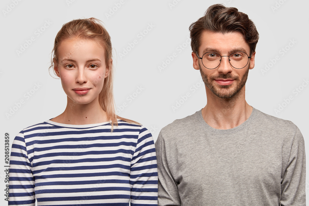 People, partnership and friendship concept. Shot of girlfriend and boyfriend stand next to each other, have pleased serious expressions, spend leisure time at home, watch interesting exciting movie People, partnership and friendship concept. Shot of girlfriend and boyfriend stand next to each other, have pleased serious expressions, spend leisure time at home, watch interesting exciting movie