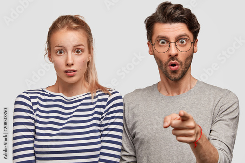 Photo of amazed hipster male indicates at camera with fore finger, shows thin...