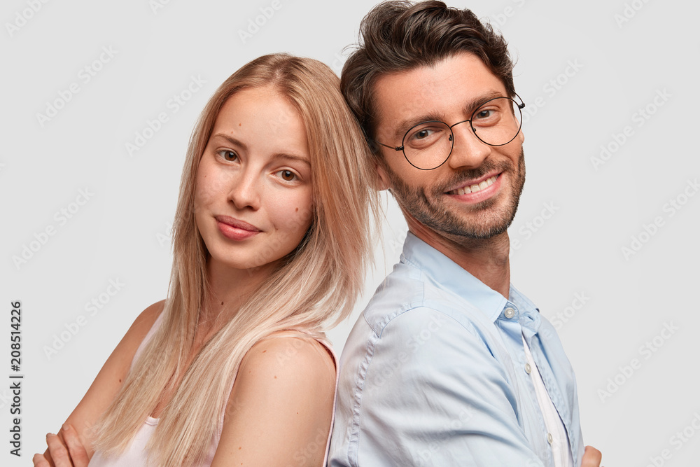 Close up portrait of lovely family couple stand back to back, pose for making shared photo, pose together against white background. Cute girl feels support of her husband. People and love concept Close up portrait of lovely family couple stand back to back, pose for making shared photo, pose together against white background. Cute girl feels support of her husband. People and love concept