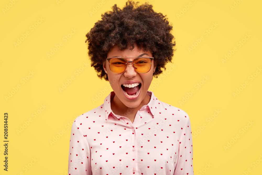 Annoyed African American female freaks out and excliams angrily, being depressed as has many work and deadlines, wears stylish clothes, isolated over yellow background. Negative emotions concept Annoyed African American female freaks out and excliams angrily, being depressed as has many work and deadlines, wears stylish clothes, isolated over yellow background. Negative emotions concept