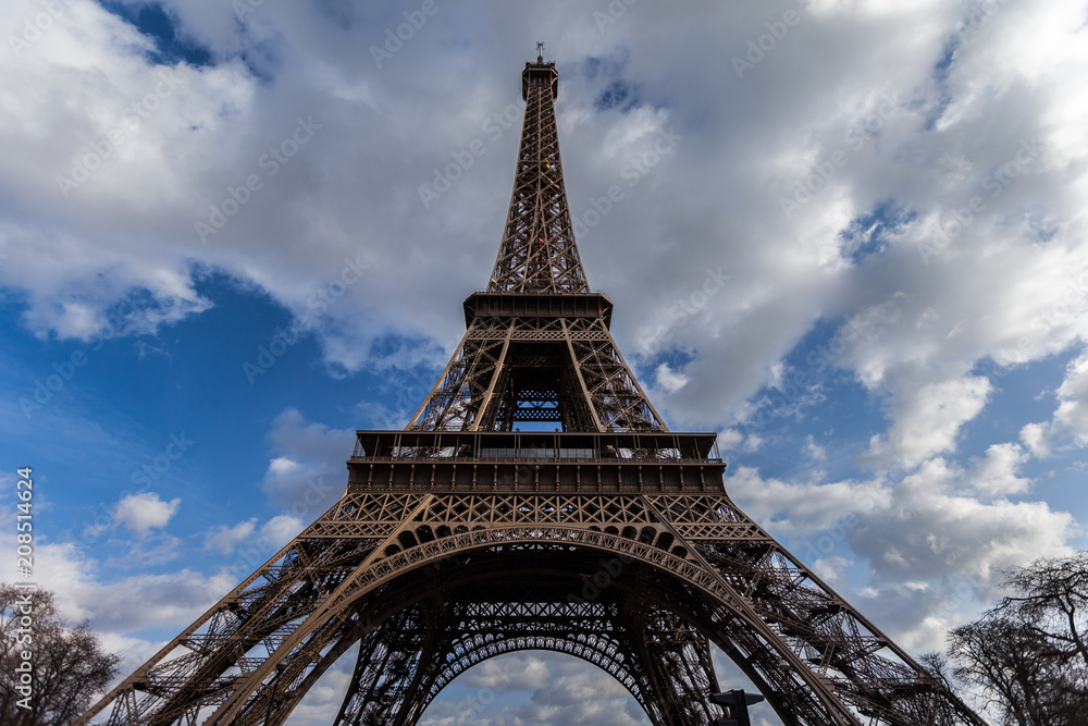 Wide angle view of iconic Eiffel tower with dramatic cloudy blue sky in the background.