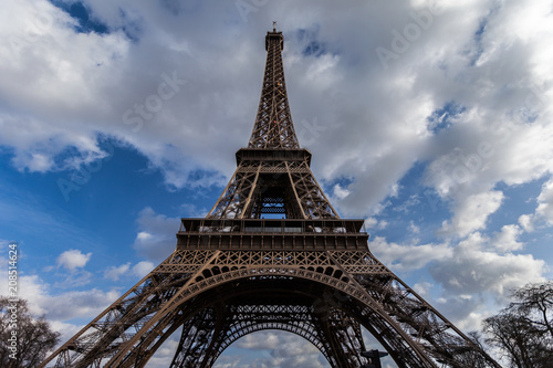 Wide angle view of iconic Eiffel tower with dramatic cloudy blue sky in the background.