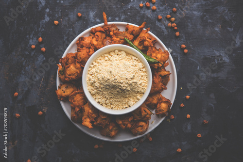 Chick pea flour or Besan powder in a ceramic or wooden bowl along with fried onion pakora or kanda bajji photo