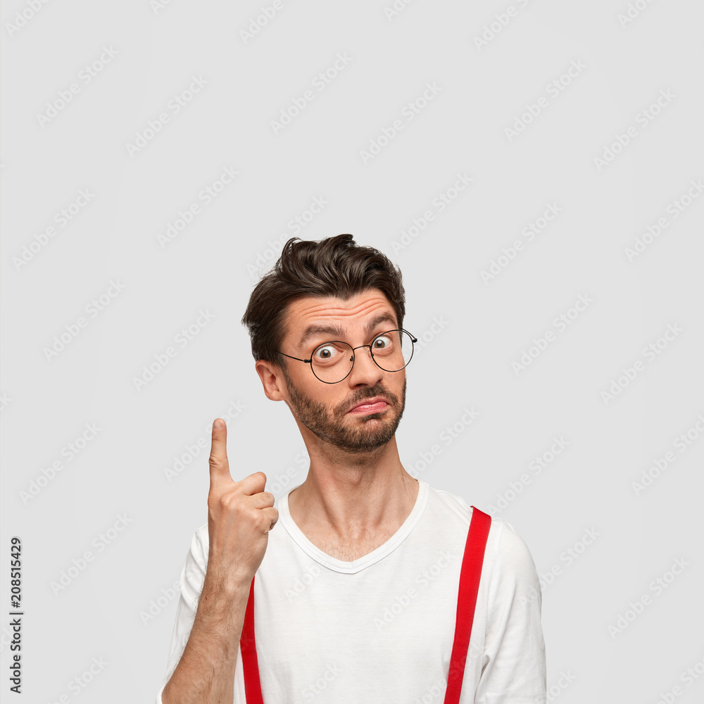 Intelligent male student has brilliant solution in mind, raises fore finger, looks with proud and confident expression at camera, wears fashionable clothes, isolated on white background, blank space Intelligent male student has brilliant solution in mind, raises fore finger, looks with proud and confident expression at camera, wears fashionable clothes, isolated on white background, blank space