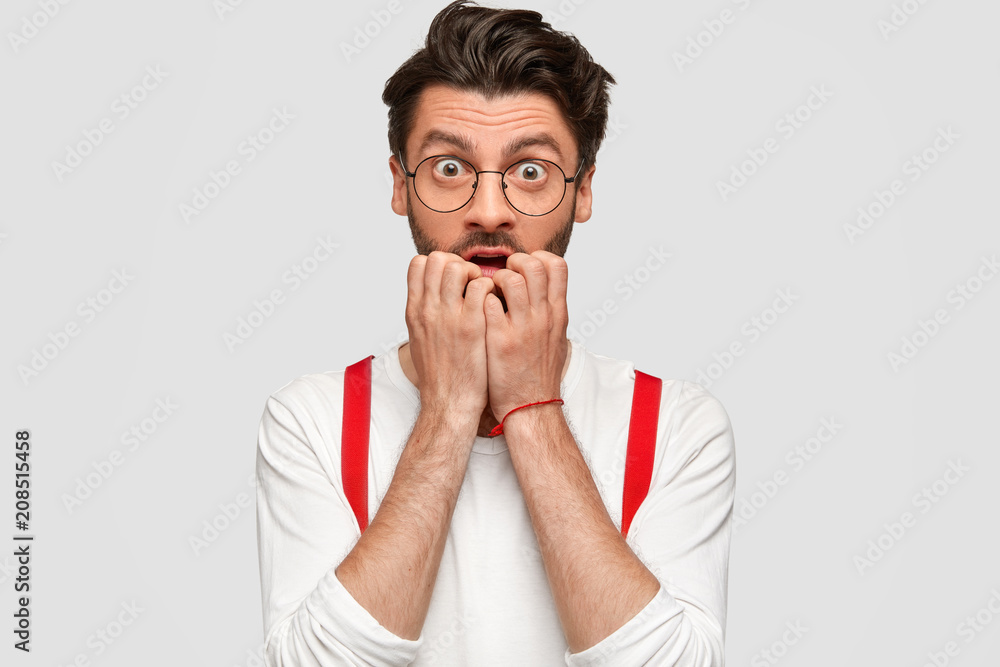 Portrait of worried scared male has nervous expression, bites finger nails, feels anxious after revealing secret, expresses surprisement and disbelief, being very emotional, has trendy hairstyle Portrait of worried scared male has nervous expression, bites finger nails, feels anxious after revealing secret, expresses surprisement and disbelief, being very emotional, has trendy hairstyle