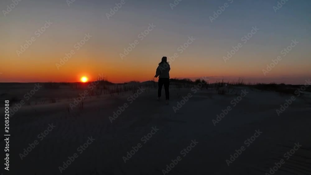 Young woman silhouetted against sunset while walking on the beach, in slow motion. Young woman silhouetted against sunset while walking on the beach, in slow motion.