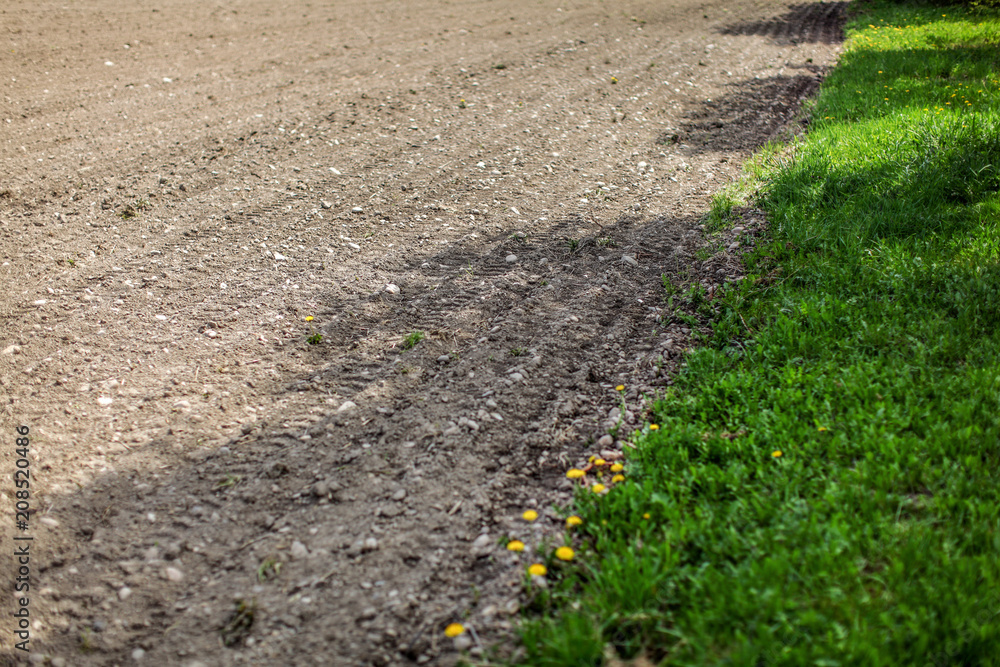 Dry field on a spring day, some tractor wheel print in ground, ready to be plowed, green meadow with dandelions next to it. Dry field on a spring day, some tractor wheel print in ground, ready to be plowed, green meadow with dandelions next to it.