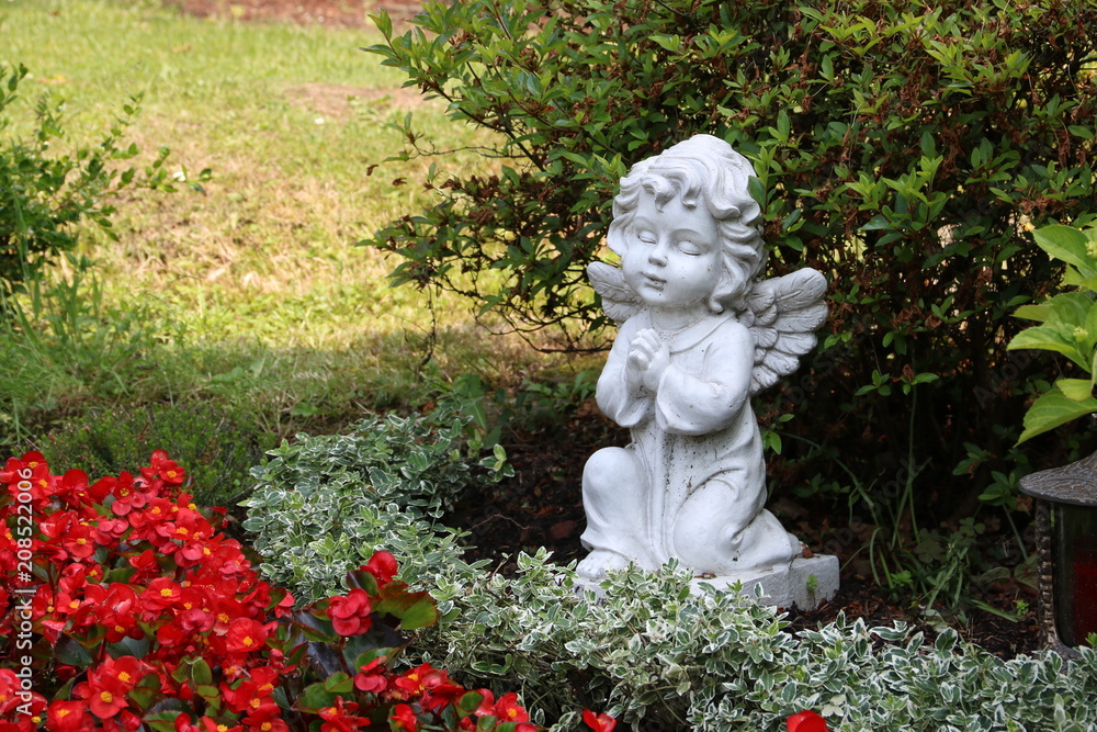 Grabengel zwischen Blumen auf dem Friedhof Grabengel zwischen Blumen auf dem Friedhof