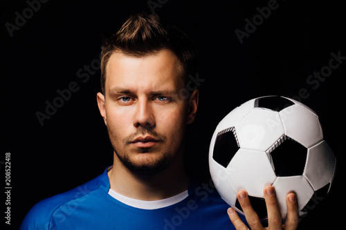 Close-up portrait of young handsome football player soccer posing on dark background. © photominus21