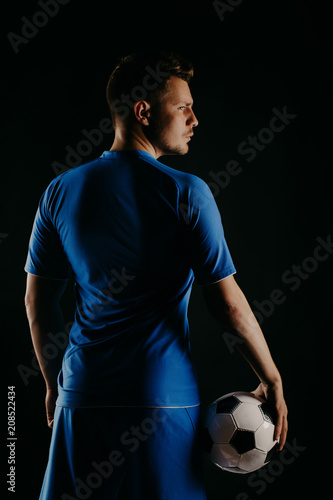 Young soccer player with ball on black background in studio.