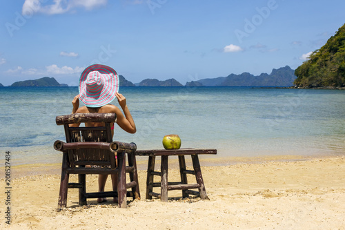 A girl sitting on a bamboo chair on the beach on a blue sea and sky background. place for text.