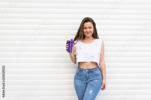 Cheerful young woman in denim jeans and crop top with pom poms holding a takeaway cup, Natural lighting, no retouch.
