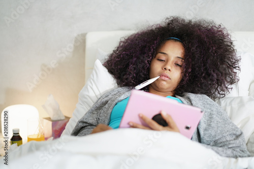 Girl With Fever Using Thermometer And Tablet In Bed