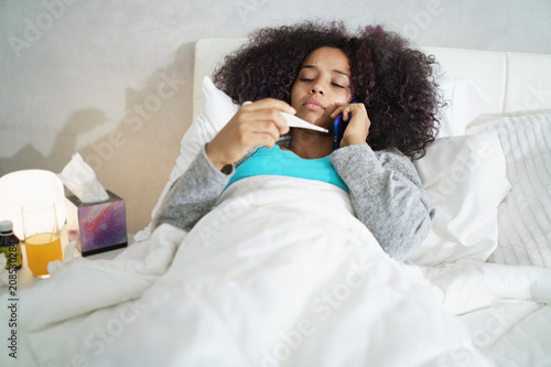 Woman With Fever Using Thermometer And Calling Doctor By Phone photo