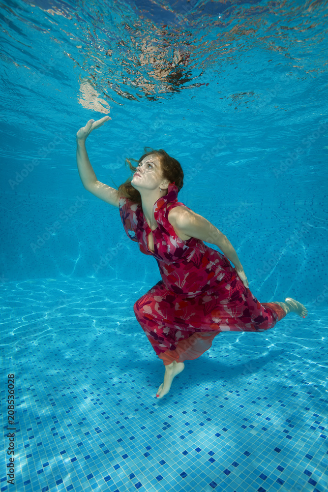 Young pregnant woman in red dress underwater in the pool