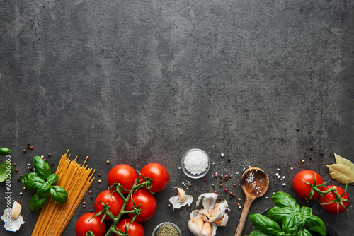 Food background for tasty Italian dishes with tomato. Various cooking ingredients with spaghetti and spoon. Top view with copy space.