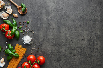 Food background for tasty Italian dishes with tomato. Various cooking ingredients with spaghetti and spoon. Top view with copy space.