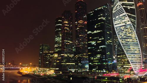 Night aerial shot of Moscow-city business towers with luminous windows. City traffic on the waterfront. Flashing lights of night city illumination.
