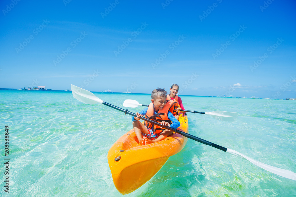 Happy boy and girl kayaking at tropical sea on yellow kayak