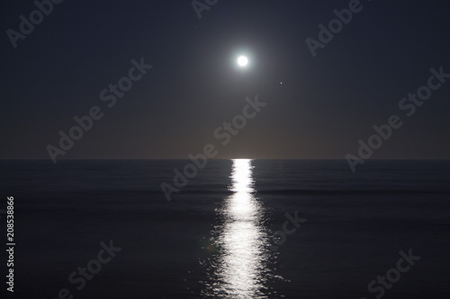 Big full moon is rising above the sea at night. Lunar light reflected on the water. Lunar path. Ocean.