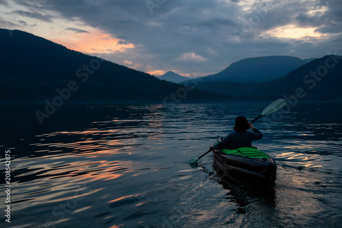 Adventurous woman kayaking during a vibrant sunset surrounded by Canadian Mountain Landscape. Taken in Howe Sound  North of Vancouver  BC  Canada.