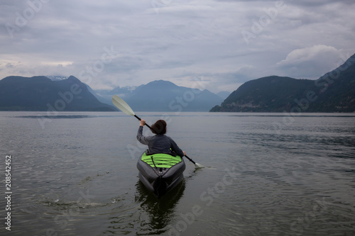 Woman kayaking around the beautiful Canadian Mountain Landscape during a vibrant cloudy evening. Taken in Howe Sound  North of Vancouver  British Columbia  Canada.
