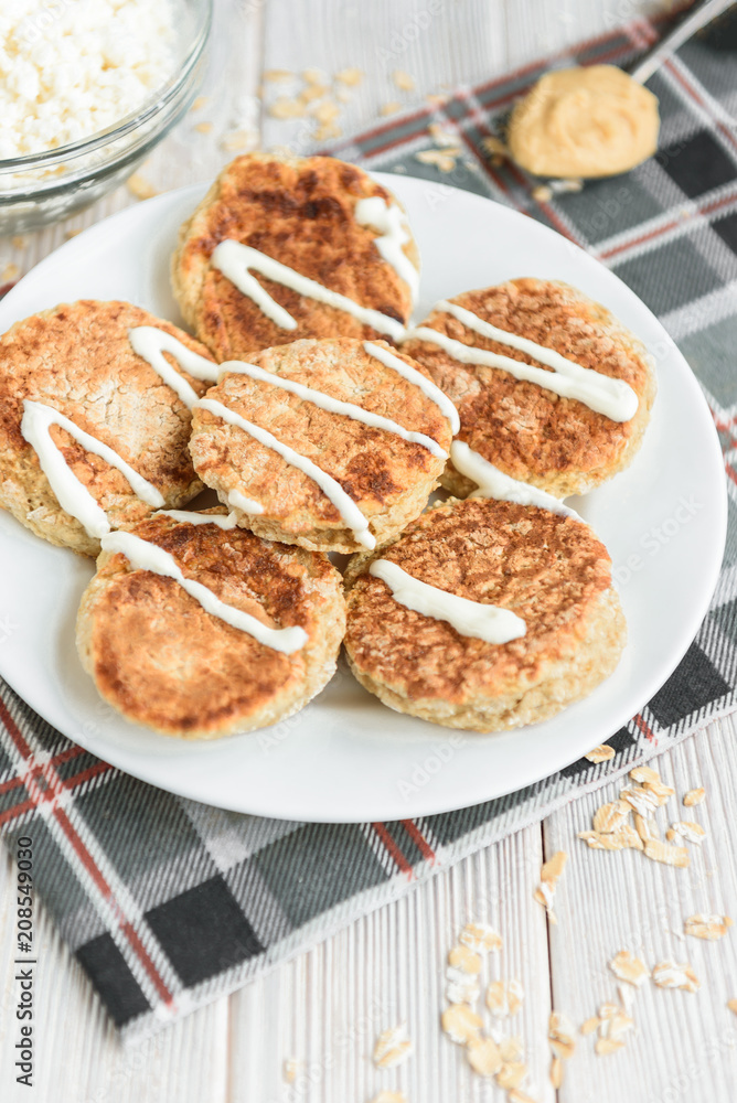 Oat cottage cheese pancakes with sour cream and peanut butter on white wooden background. Healthy breakfast, snack or diner.