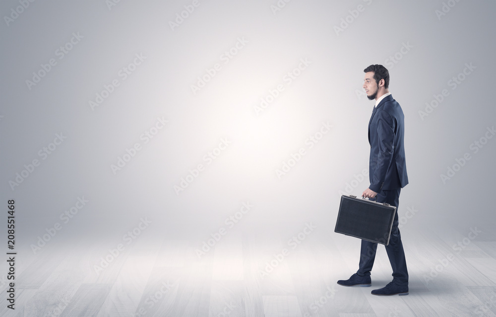 Successful businessman walking in front of an empty wall with briefcase on his hand
Successful businessman walking in front of an empty wall with briefcase on his hand