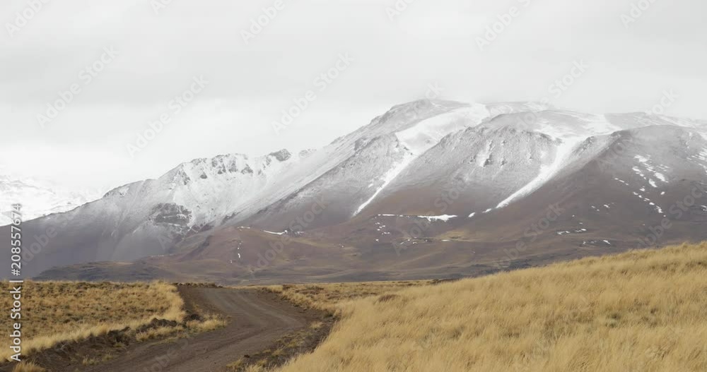 Lanscape of grasslands in an altiplain of Domuyo Volcano surroundings. Gravel road. Snowy Domuyo Volcano at background. Winter cold scene camera stays still while clouds move along the mountain Lanscape of grasslands in an altiplain of Domuyo Volcano surroundings. Gravel road. Snowy Domuyo Volcano at background. Winter cold scene camera stays still while clouds move along the mountain