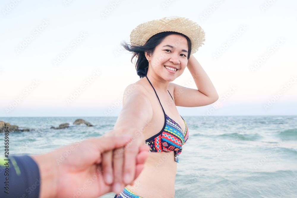 Fashion photo of beautiful asian women leading man hand to sea