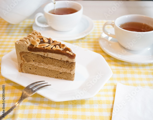 Afternoon tea. Sea salt caramel almond coffee cake serves with cup of teas. Blurred teapot is pouring tea on the background.