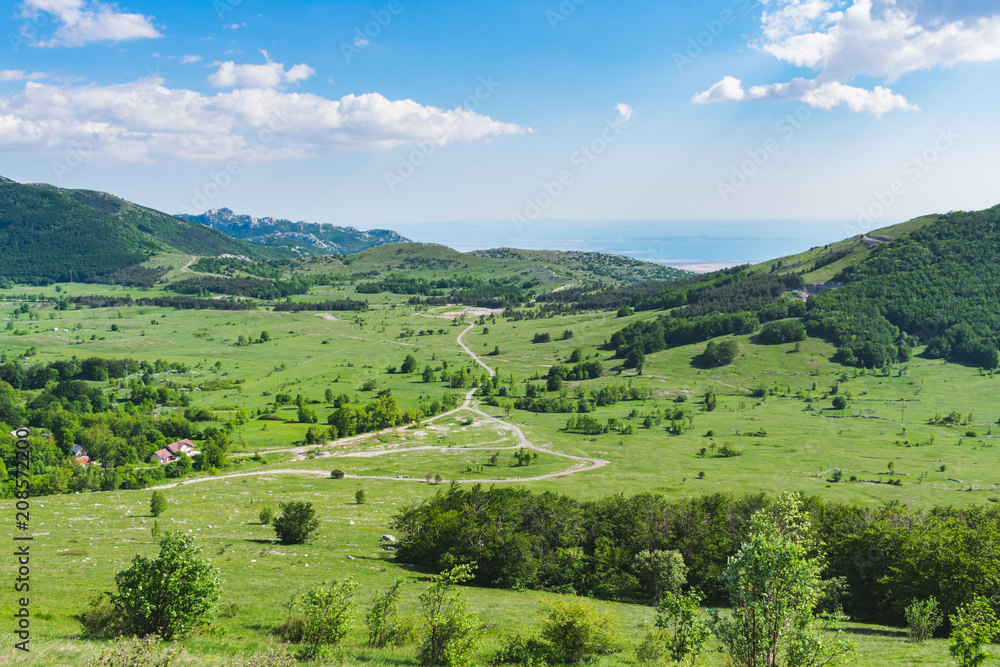 A beautiful landscape view over a mountain valley and forested mountain peaks of Velebit mountain range in Croatia of the Adriatic sea or coastline with islands. Summer in Croatia or travel concept