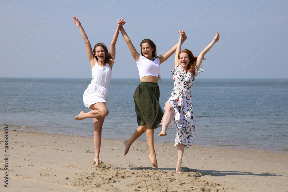 Drei hübsche jungen Frauen springen an den Händen haltend an einem Strand in die Luft
