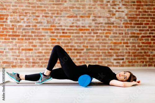 Side view of charming young woman workout with foam roller in a fitness center.