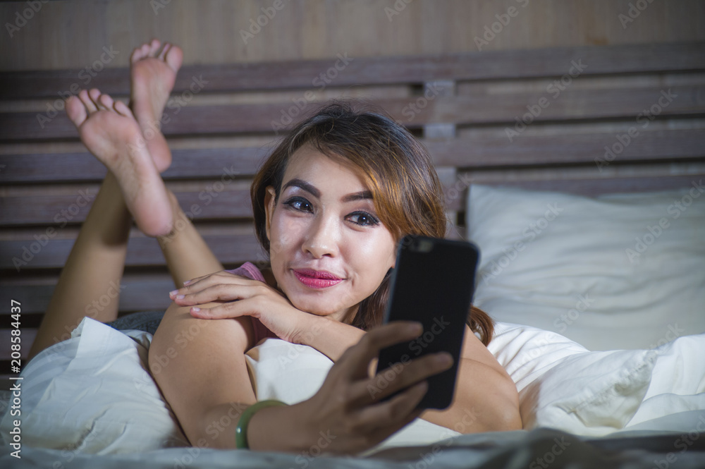young beautiful and happy woman lying on bed smiling and flirting on internet social media app using mobile phone cheerful and relaxed on her bedroom