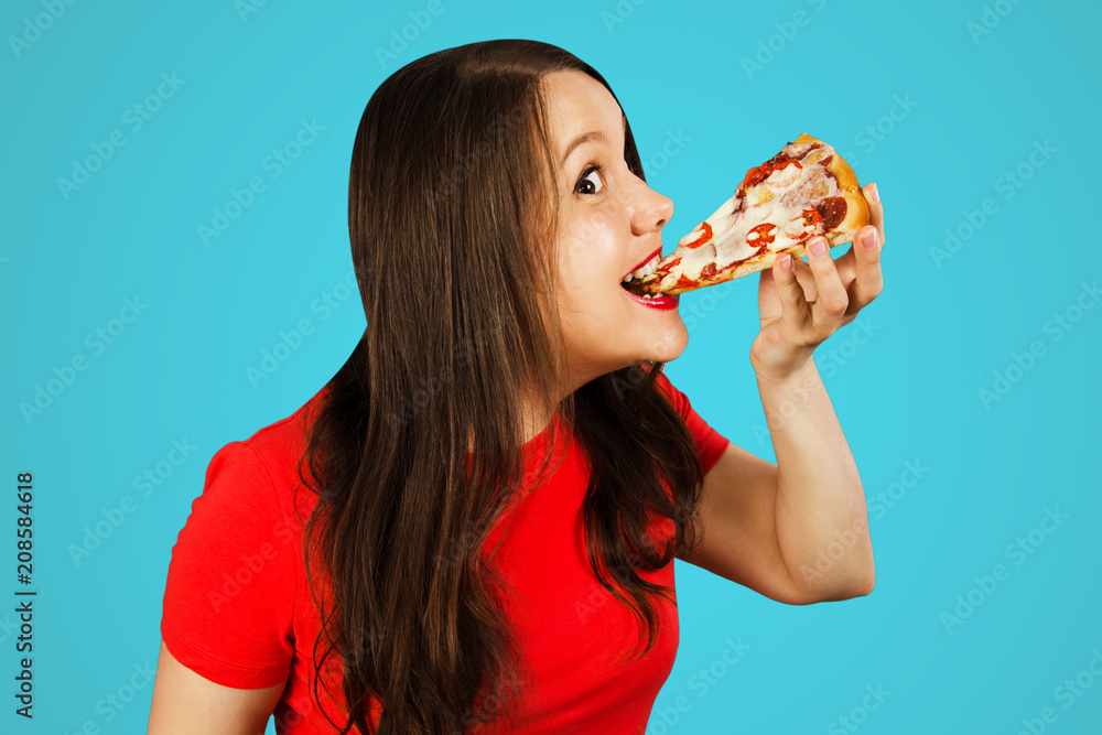 Young handsome woman eating pizza, isolated on blue background. Side view. Young handsome woman eating pizza, isolated on blue background. Side view.
