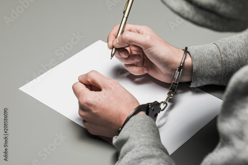 Hands of the criminal in handcuffs write a handle on paper. Sincere confession, request, statement. Justice