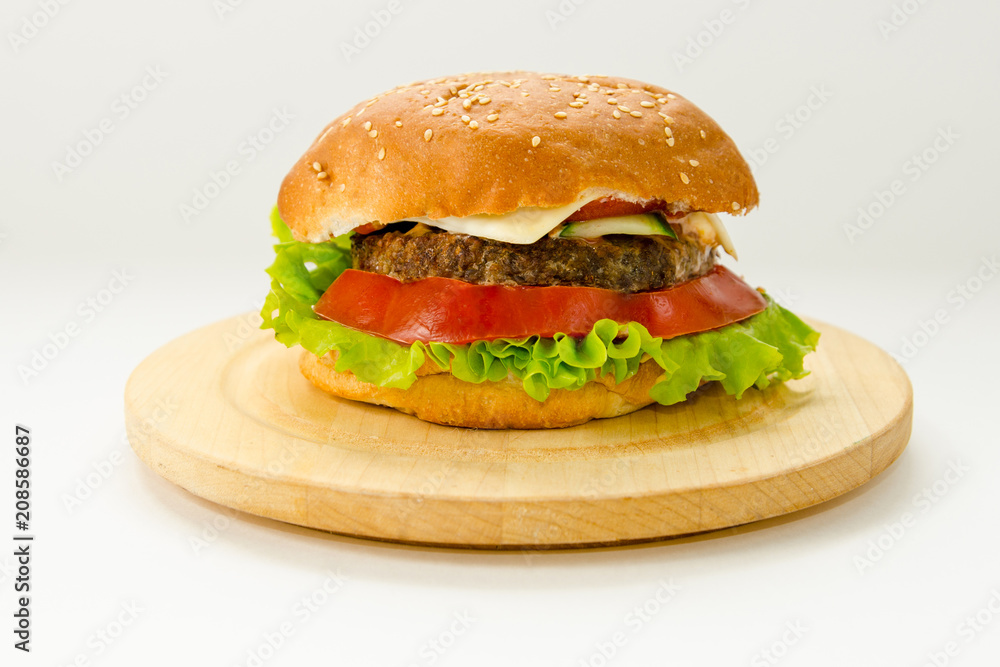 Hamburger lying on a round wooden board on a white background. Hamburger lying on a round wooden board on a white background.
