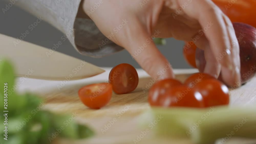 Cutting one red cherry tomatoes with kitchen knife on wooden board Cutting one red cherry tomatoes with kitchen knife on wooden board