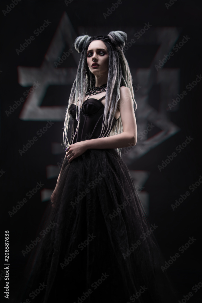 Naklejka premium Side view of woman with dreads and festive black gothic dress posing on dark background