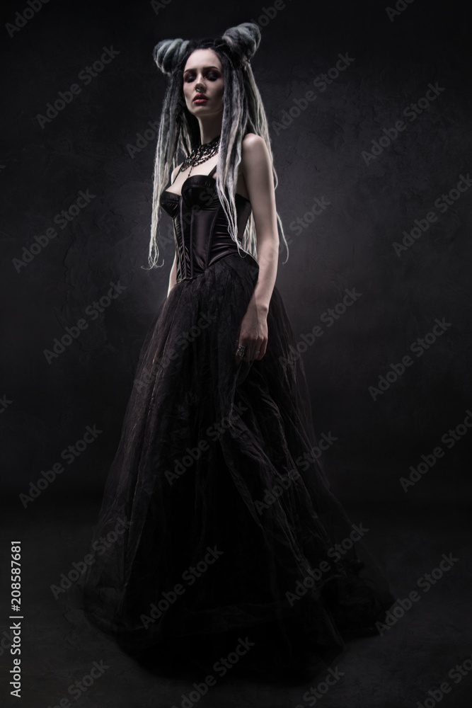 Woman with dreads and black gothic dress posing on dark background