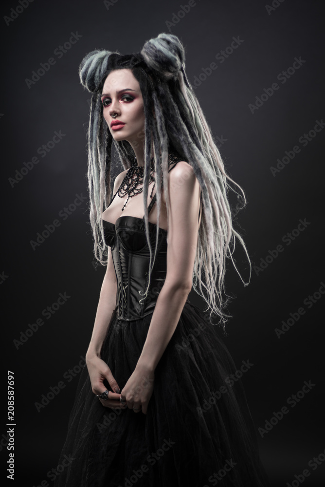 Woman with dreads and black gothic dress posing on dark background Woman with dreads and black gothic dress posing on dark background