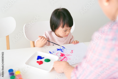 Little asian girl painting with paintbrush and colorful paints